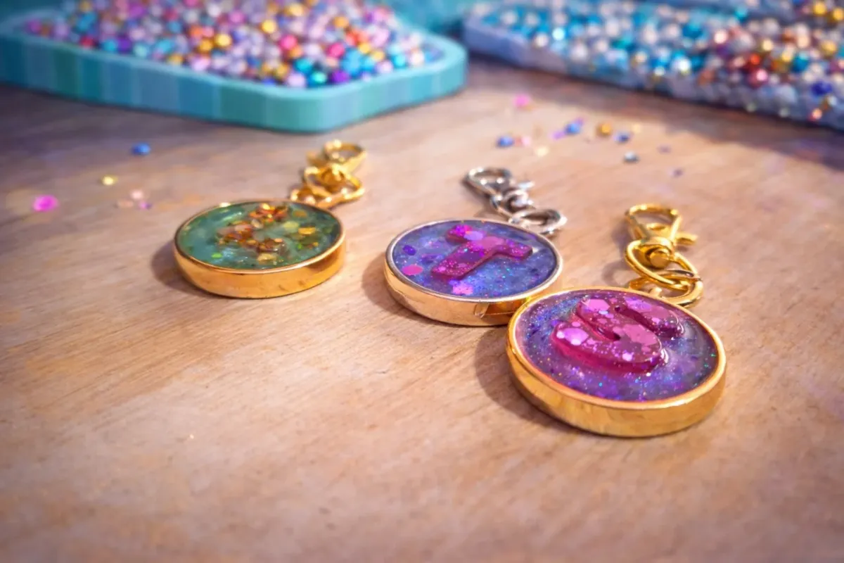 Round initial keychains in gold bezels, with a tray of glitter behind them